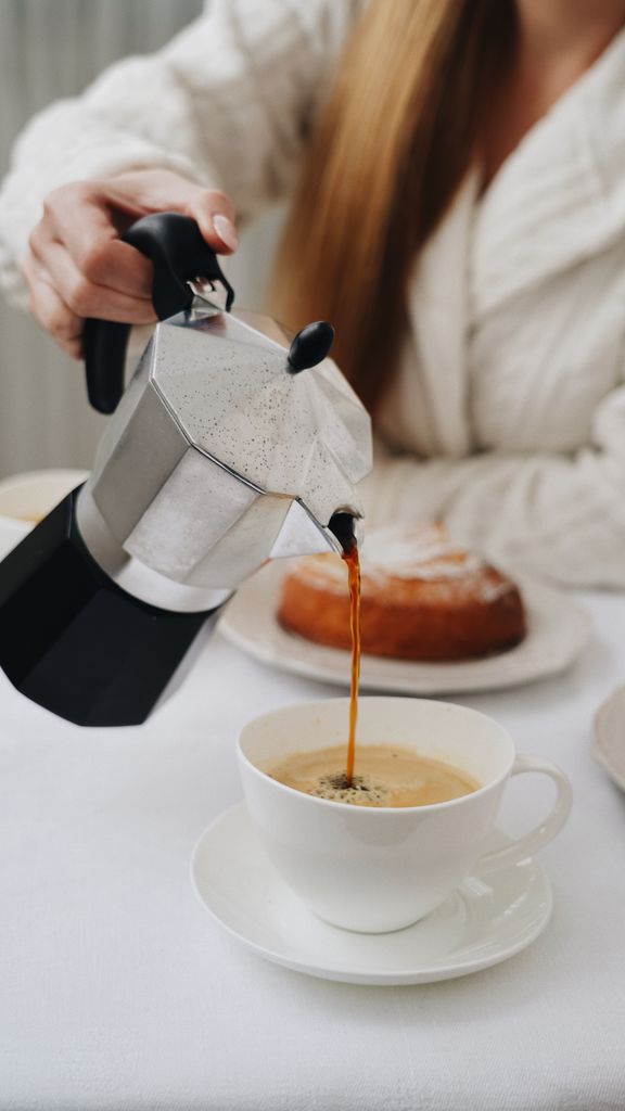 A woman pouring coffee into a cup with a pastry on the table, ideal for cafe themes.