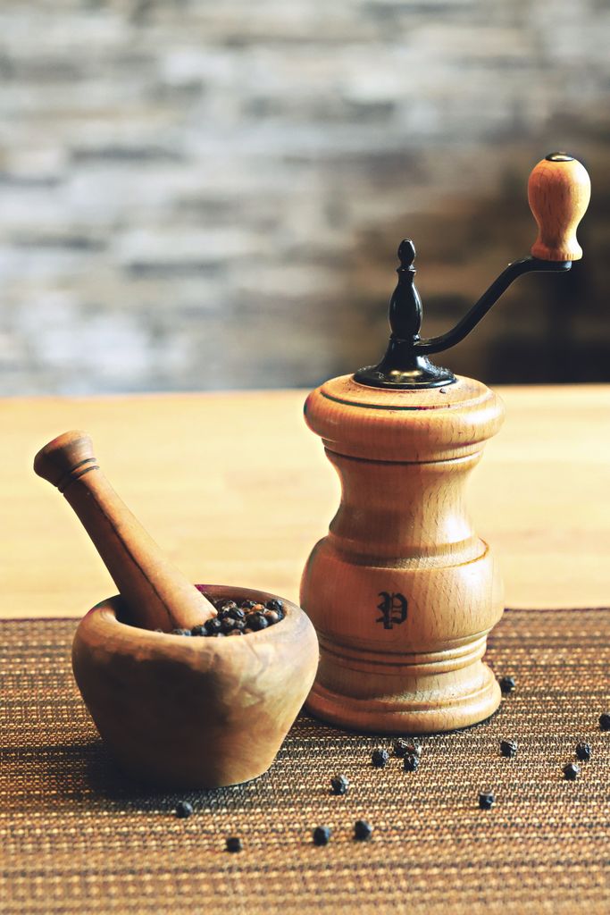 Rustic pepper mill and mortar with pestle on wooden surface.
